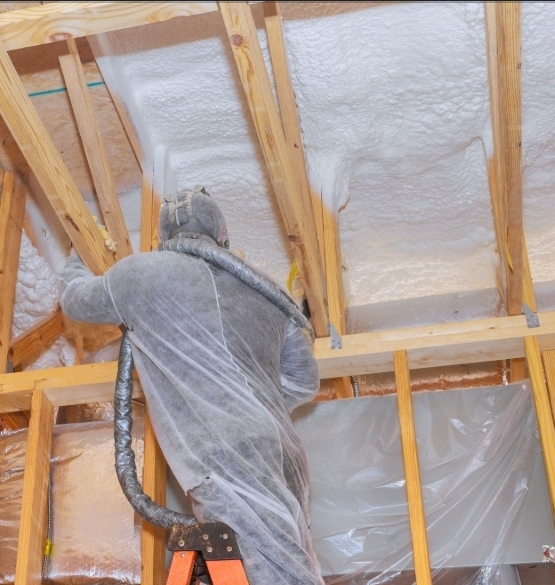 Technician applying spray-foam insulation between roof rafters